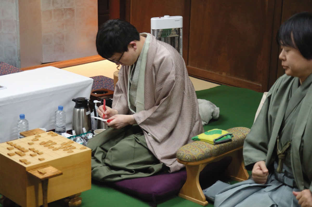 永瀬拓矢九段（左）は封じ手の入った封筒に署名する。右は立会人の藤井猛九段（日本将棋連盟提供）