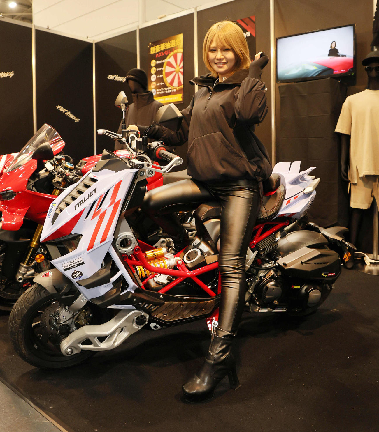 大阪モーターサイクルショー2025で、特異な形状のフロントサスを持つバイクと一緒にポーズをとるキャンペーンガール（撮影・宮崎幸一）
