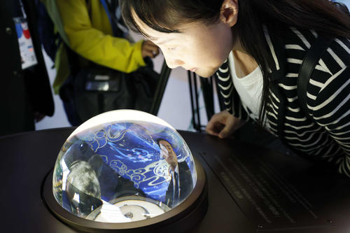 中国館で、月の裏側で採取された土の展示をのぞき込む来場者(共同)