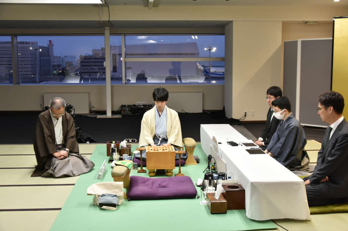 永瀬拓矢九段が封じ手を別室で書いているのを対局場で待つ立会人の中村修九段（左）と盤の奥の藤井聡太名人（日本将棋連盟提供）