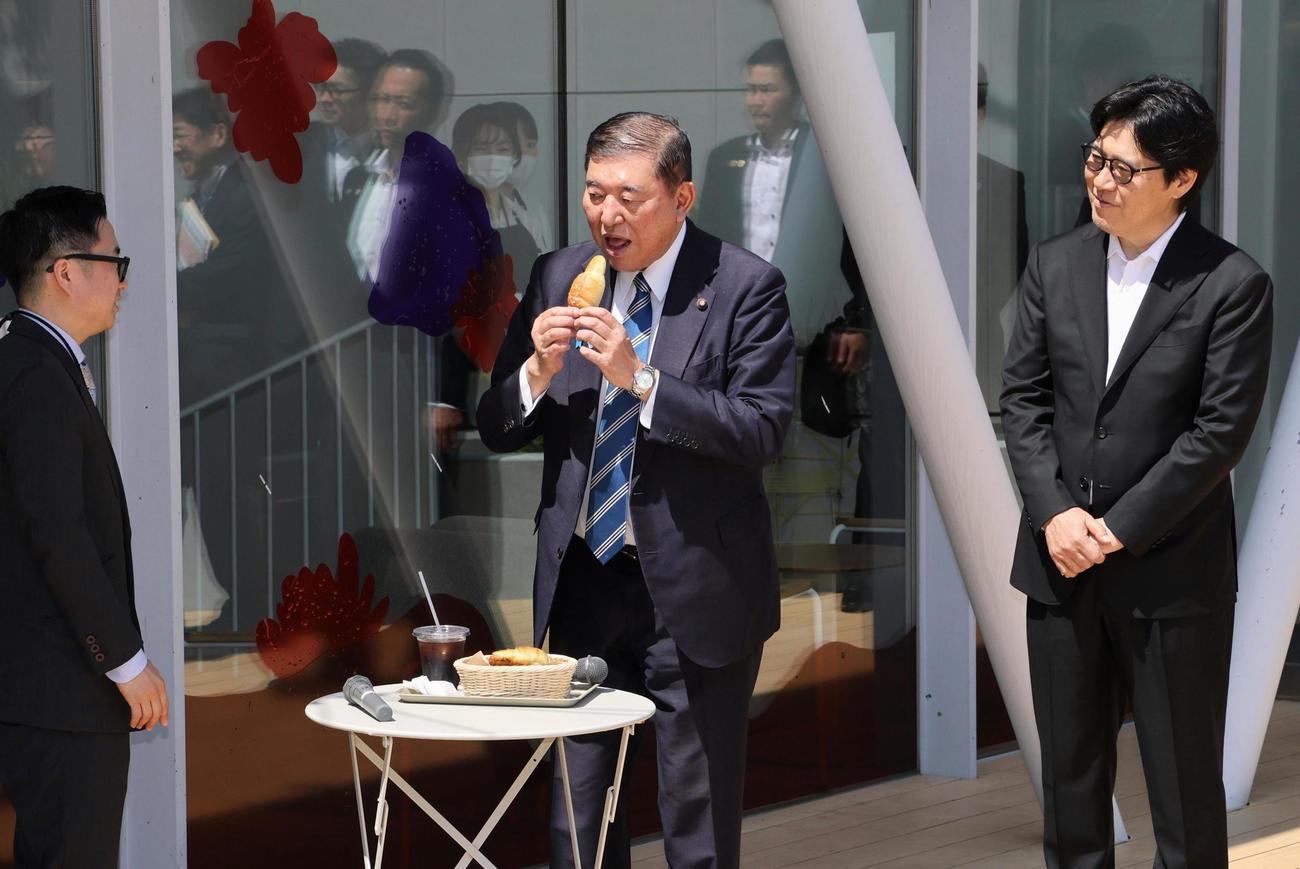 「ジンズパーク」で販売されているパンを食べる石破首相（中央）