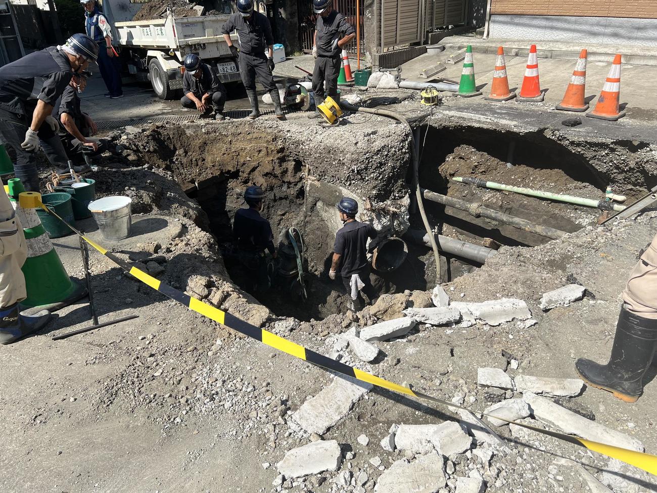 鎌倉市で、破損、漏水した水道管の修復のため、路上の大きな空洞の中で工事をする作業員