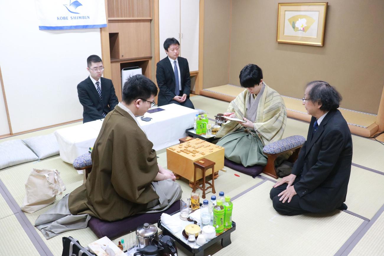 王位戦7番勝負第2局、永瀬拓矢九段（左）の封じ手にサインする藤井聡太王位（右）、中央は立会人の福崎文吾九段（日本将棋連盟提供）