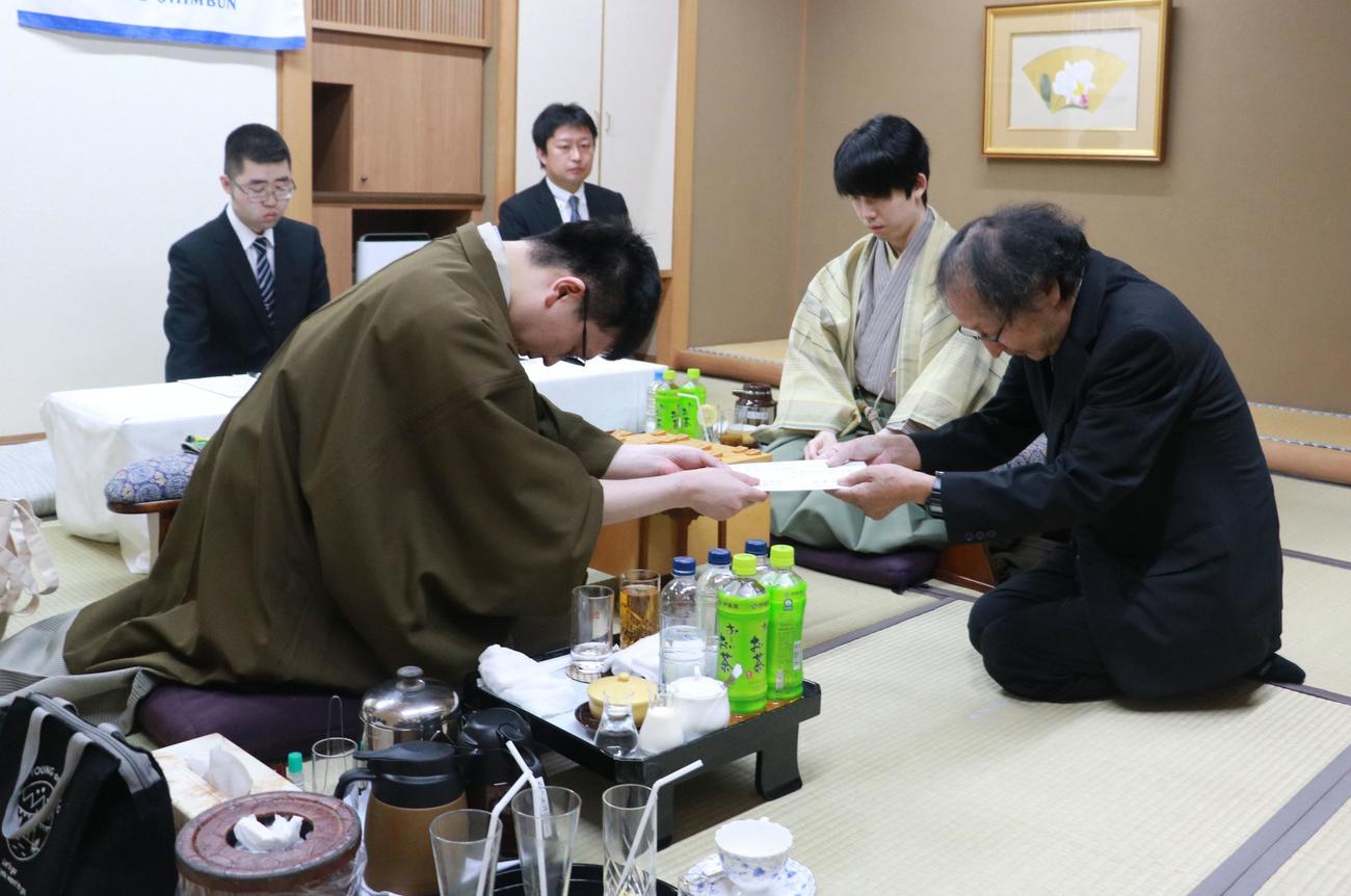 封じ手の封筒を立会人の福崎文吾九段（右）に手渡す永瀬拓矢九段（左）、中央は藤井聡太王位（日本将棋連盟提供）