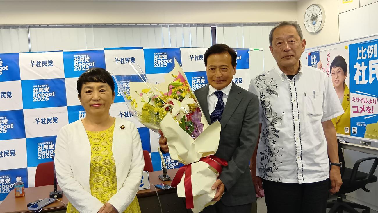 花束を手にするラサール石井氏（中）を祝福する社民党の福島瑞穂党首（左）と服部良一幹事長