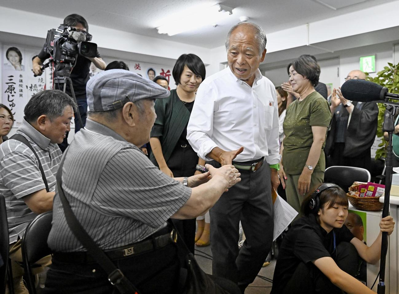 比例代表で当選が決まり、支援者（左）と握手を交わし記者会見会場に入る自民党の鈴木宗男氏。後方は長女の鈴木貴子衆院議員（共同）