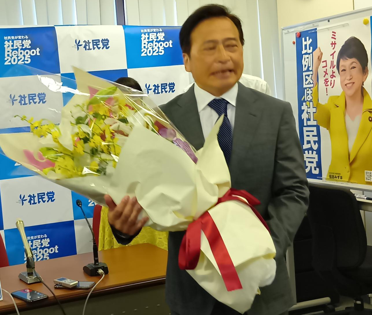 社民党本部で花束を贈られ感無量のラサール石井氏