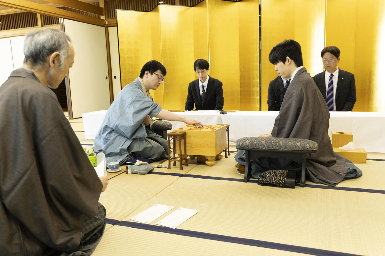 立会人の中田功八段（左）が封じ手を読み上げ、永瀬拓矢九段（中央）が駒を動かす、右は藤井聡太王位（日本将棋連盟提供）