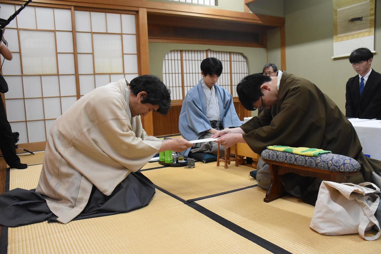 封じ手の封筒を立会人の森内俊之九段（左）に手渡す永瀬拓矢九段（右）、中央は藤井聡太王位（日本将棋連盟提供）