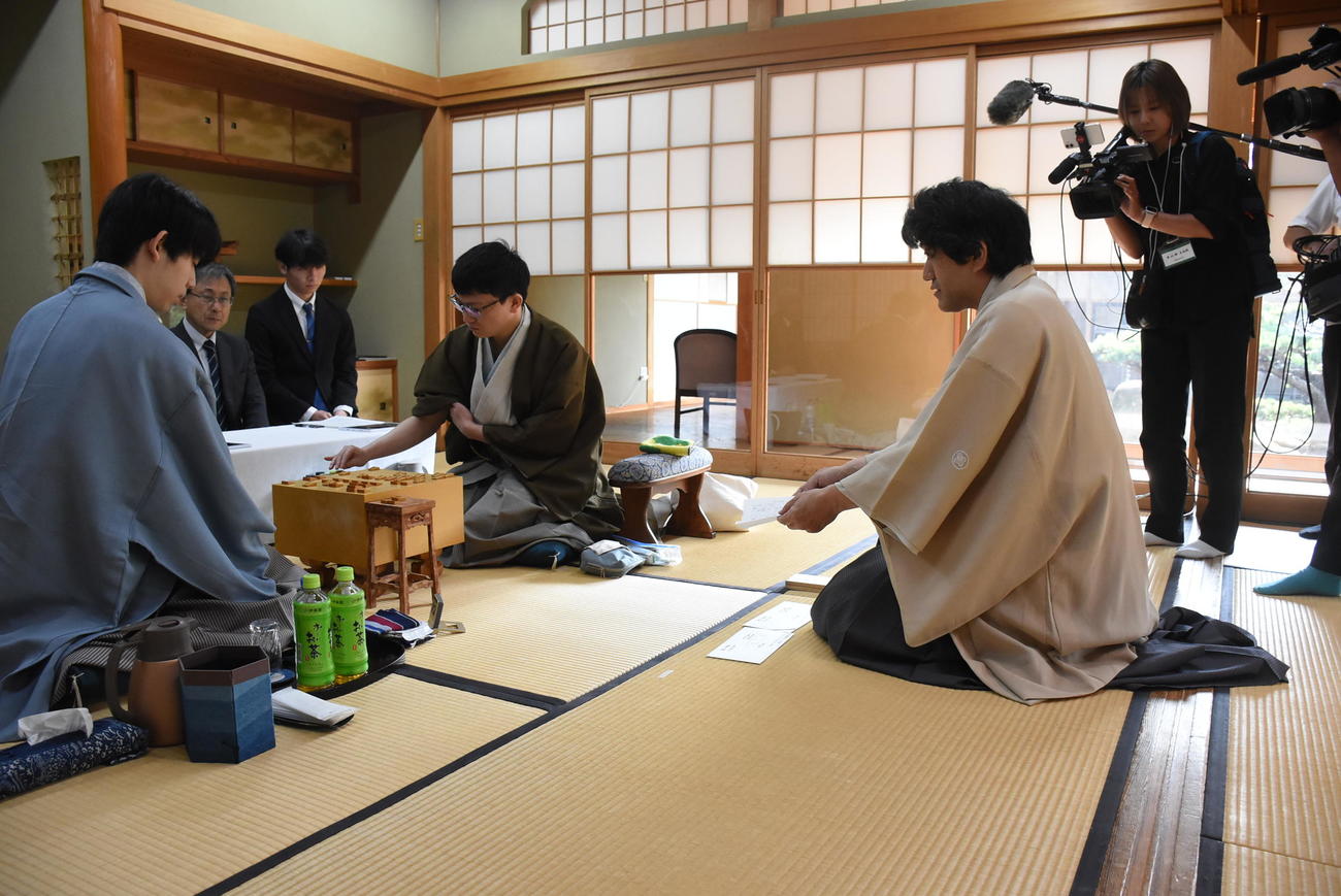 立会人の森内俊之九段（右）が示す封じ手の封筒を確認する藤井聡太王位（左）、中央は永瀬拓矢九段（日本将棋連盟提供）