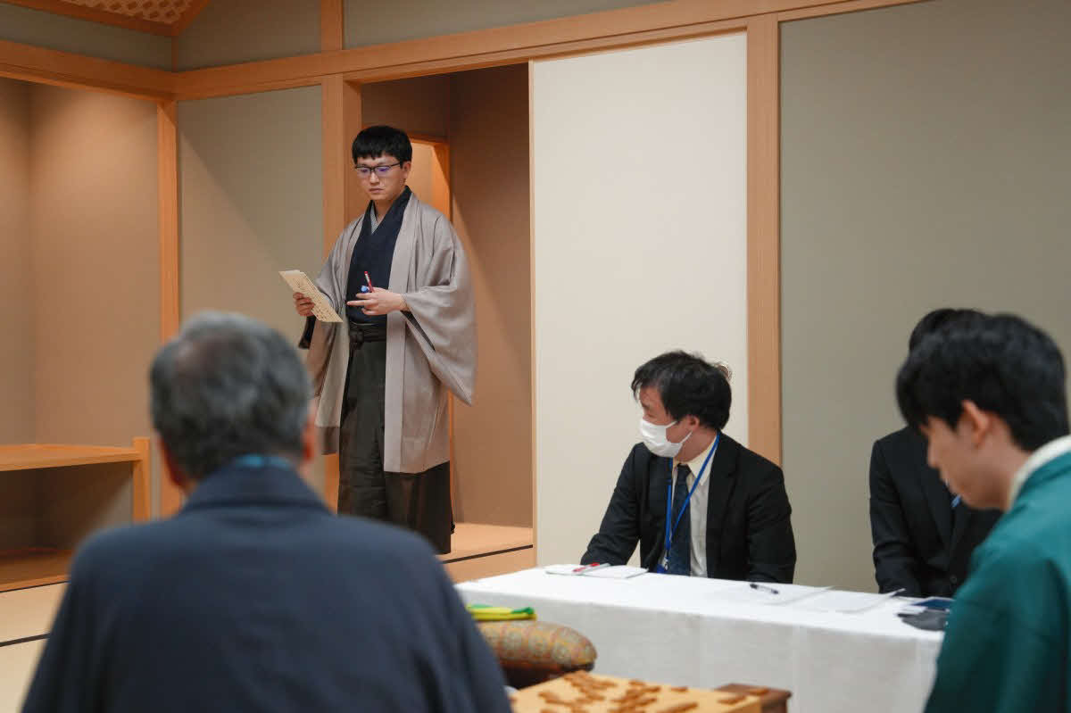 永瀬拓矢九段が封じ手を入れた封筒を持って対局室に戻る（右は藤井聡太王位、日本将棋連盟提供）