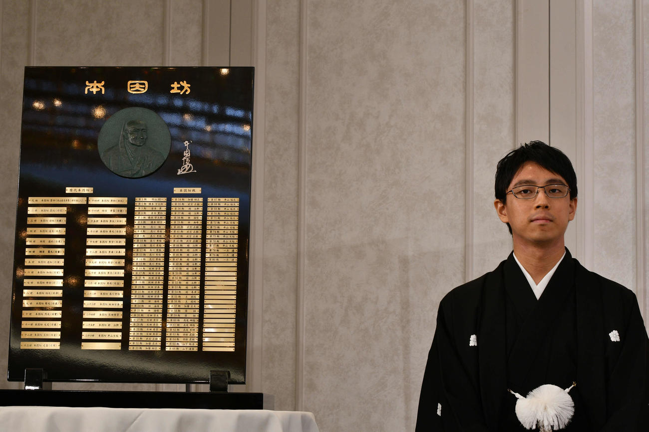歴代本因坊の名が刻まれた本因坊盾の横に就位式で着座した一力遼本因坊