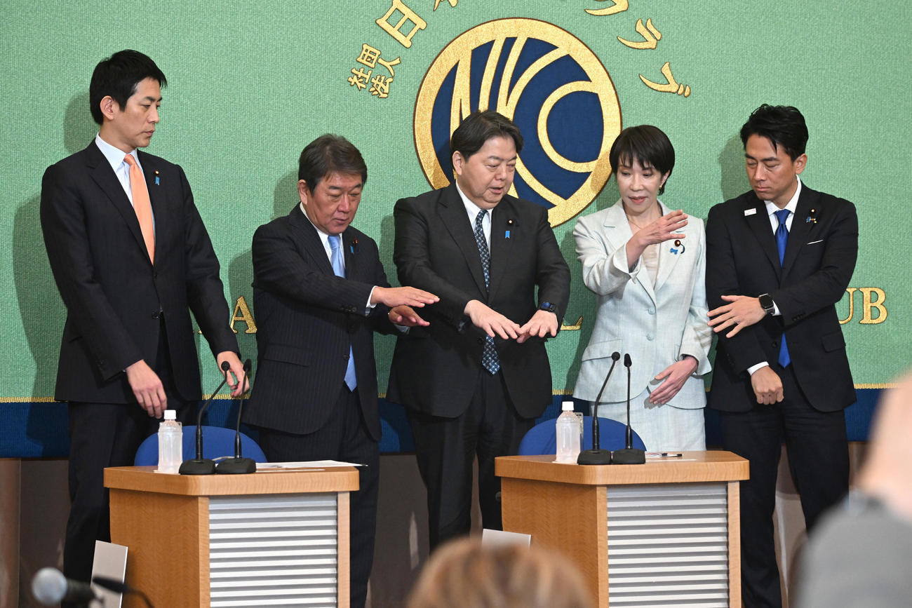 日本記者クラブ主催の討論会の冒頭、集合写真の手の組み方を話し合う（左から）小林鷹之元経済安保相、茂木敏充前幹事長、林芳正官房長官、高市早苗前経済安保相、小泉進次郎農水相（代表撮影）