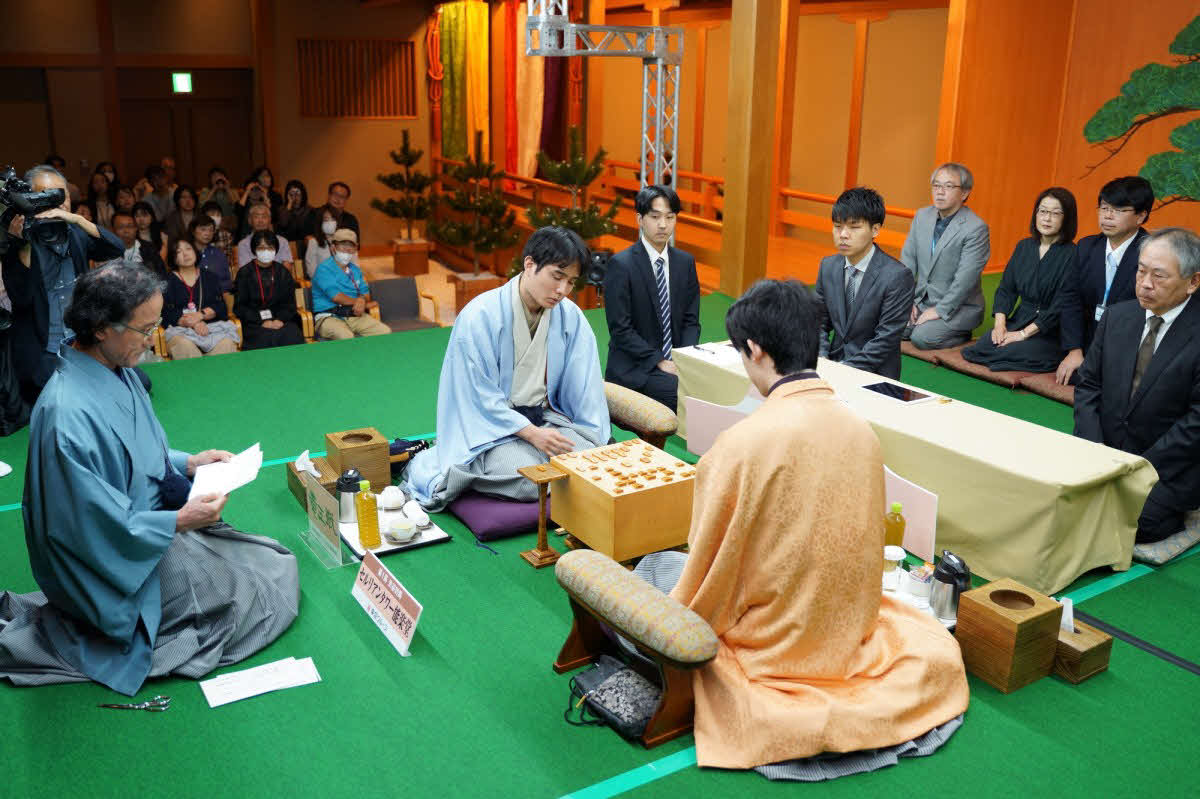 竜王戦第1局は立会人の深浦康市九段（左）が佐々木勇気八段（中央）の封じ手を開封して2日目を再開（日本将棋連盟提供）