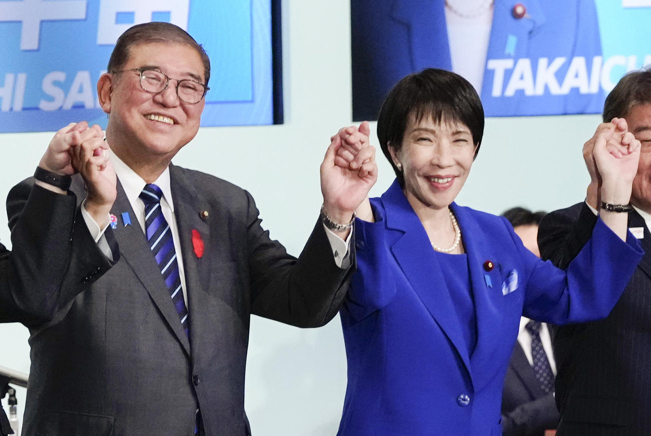 自民党総裁選後に開かれた両院議員総会で、石破首相（左）らと手を取り合う高市早苗新総裁（共同）