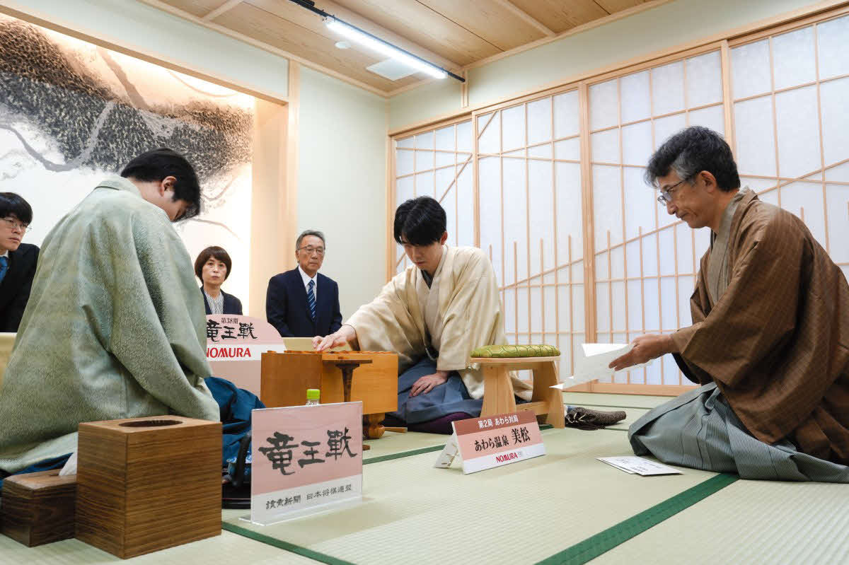 佐々木勇気八段（左）が藤井聡太竜王（中央）に挑戦する竜王戦7番勝負第2局は立会人の佐藤康光九段（右）が封じ手を示して2日目を再開（日本将棋連盟提供）