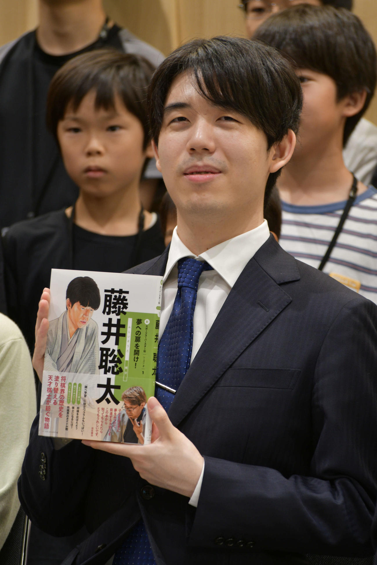 子どもたちののあこがれや目標となる児童書「新スポーツスーパースター伝　藤井聡太」を手にする藤井聡太7冠