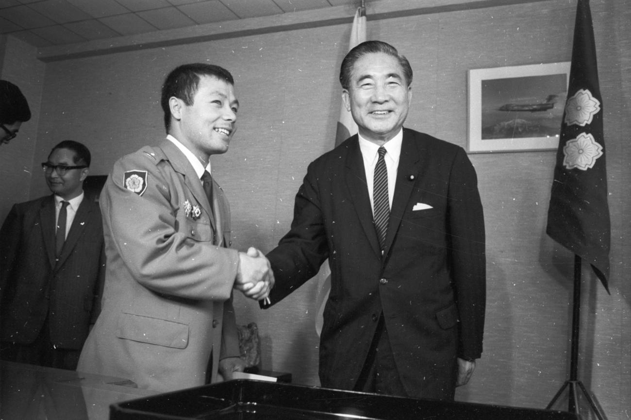 1964年10月15日、日本人金メダル第1号の自衛隊体育学校、三宅義信3尉（左＝重量挙げフェザー級）に対し、小泉純也防衛庁長官（右）から「第1級防衛功労章」（副賞1万8000円）が贈られた。小泉長官は、小泉純一郎の父、小泉進次郎の祖父