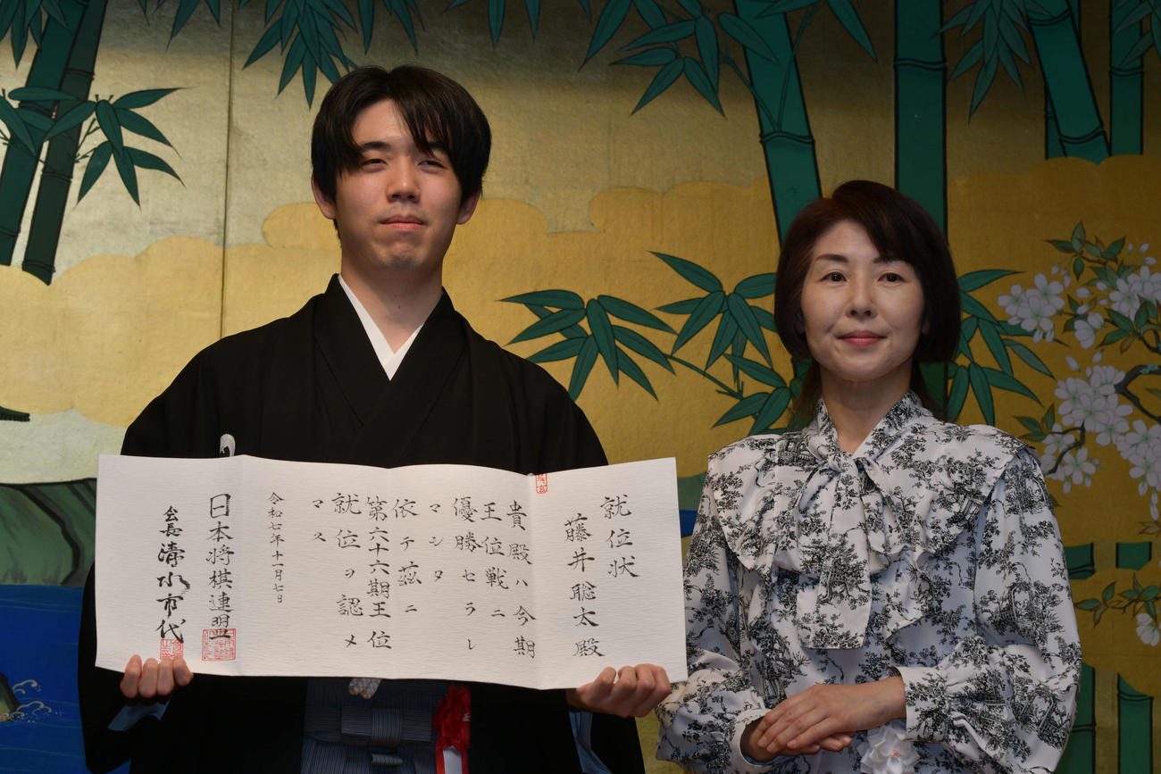 藤井聡太王位（左）は就位式で日本将棋連盟の清水市代会長（右）から渡された就位状を手にする