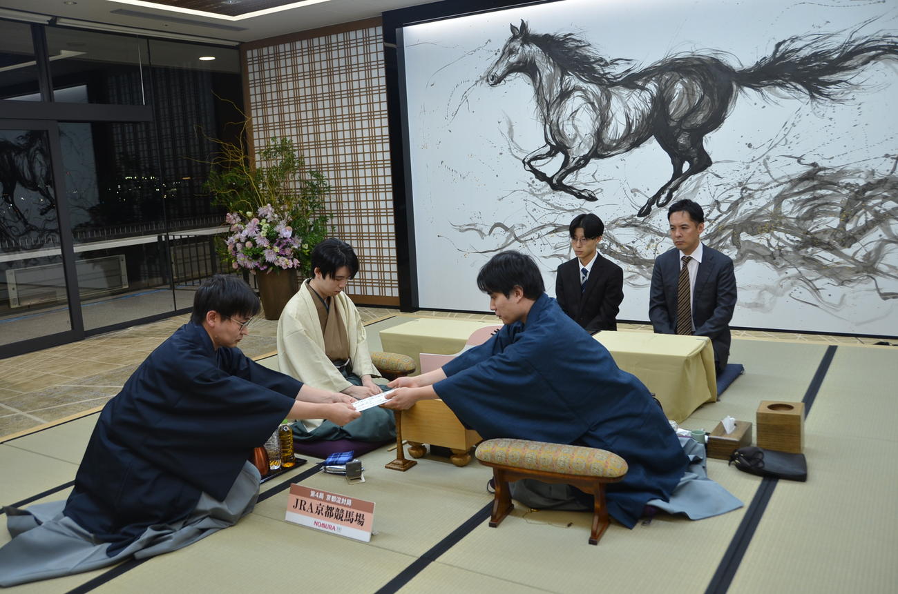 封じ手の封筒を立会人の山崎隆之九段（左）に手渡す佐々木勇気八段（右）、中央は藤井聡太竜王（日本将棋連盟提供）