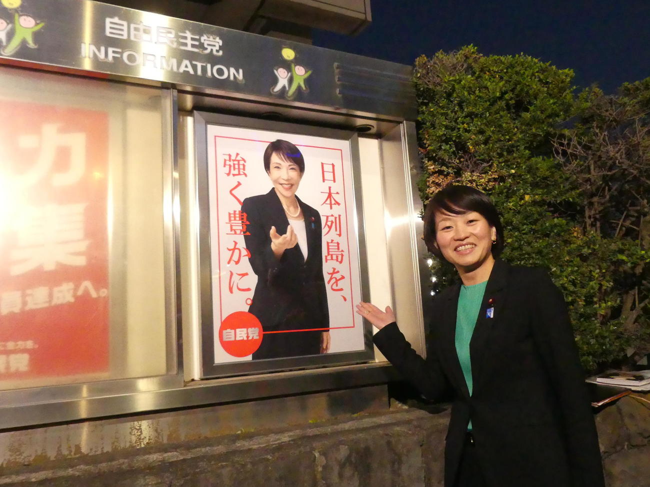 自民党本部前の掲示板に、完成したばかりの高市早苗総裁のポスターを張り笑顔をみせる鈴木貴子広報本部長（撮影・中山知子）