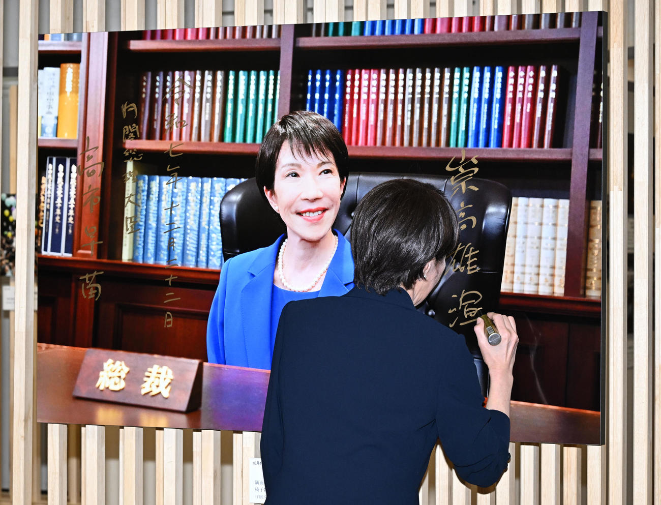 「2025年報道写真展」で本紙・江口和貴カメラマンが撮影した自民党総裁の椅子に座る自身の写真にサイン、「崇高雄渾」と記す高市首相（撮影・千葉一成）