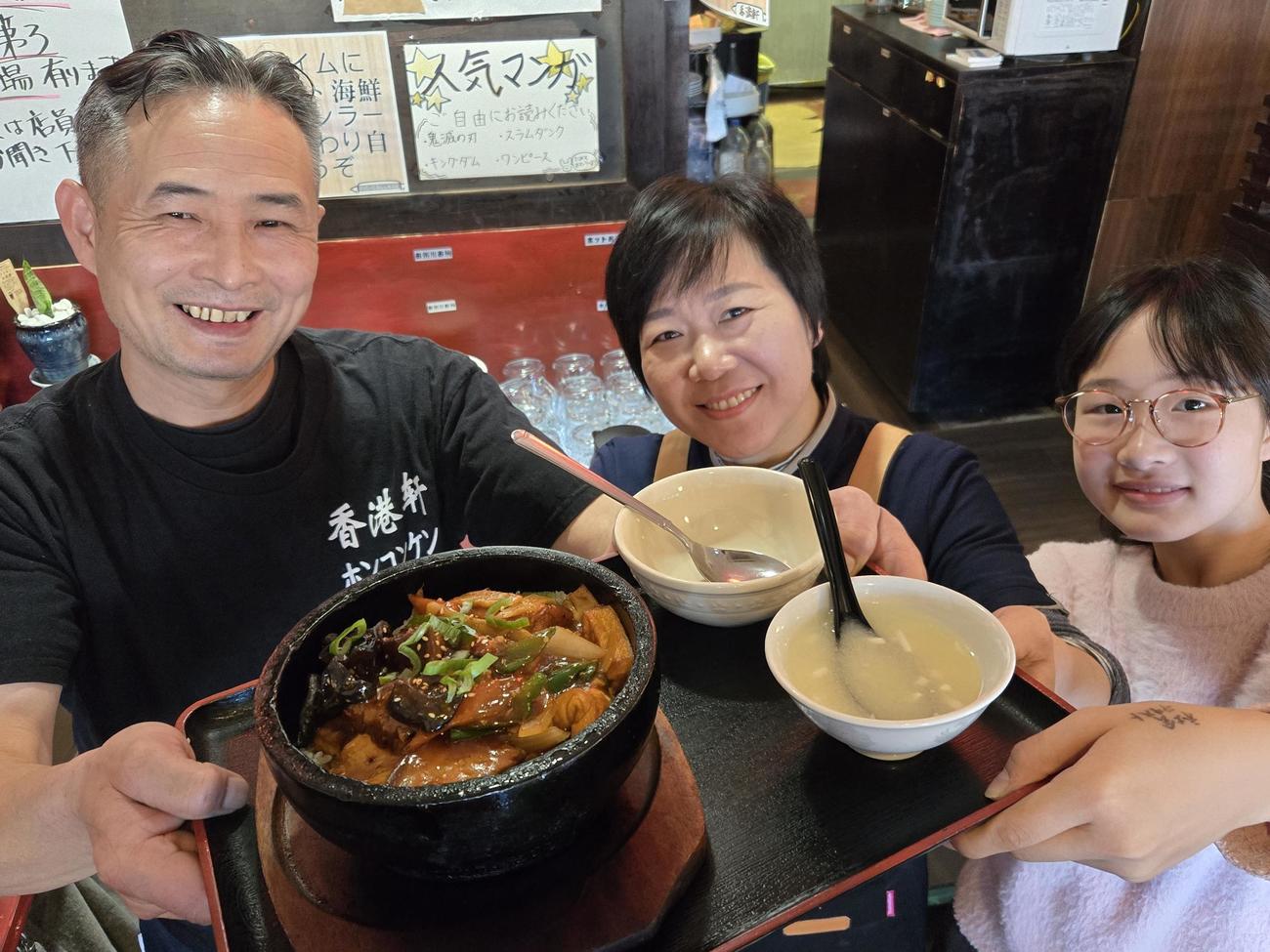 沿道で応援する人を応援するアゲアゲメニュー「揚げ豆腐の五目あんかけ石焼きご飯」を掲げる料理人の徐建華さんと奥さんの劉燕さん、長女の徐紫棋さん