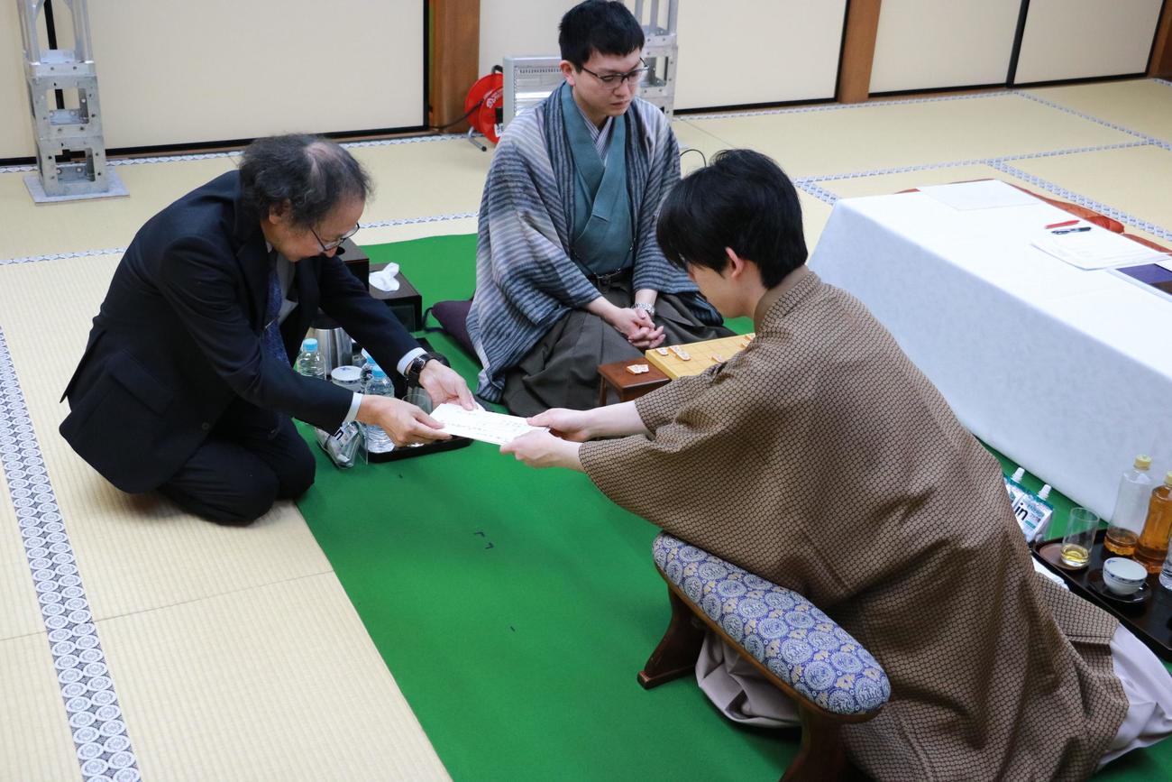 封じ手の封筒を立会人の福崎文吾九段に手渡す藤井聡太王将（右）、中央は永瀬拓矢九段（日本将棋連盟提供）