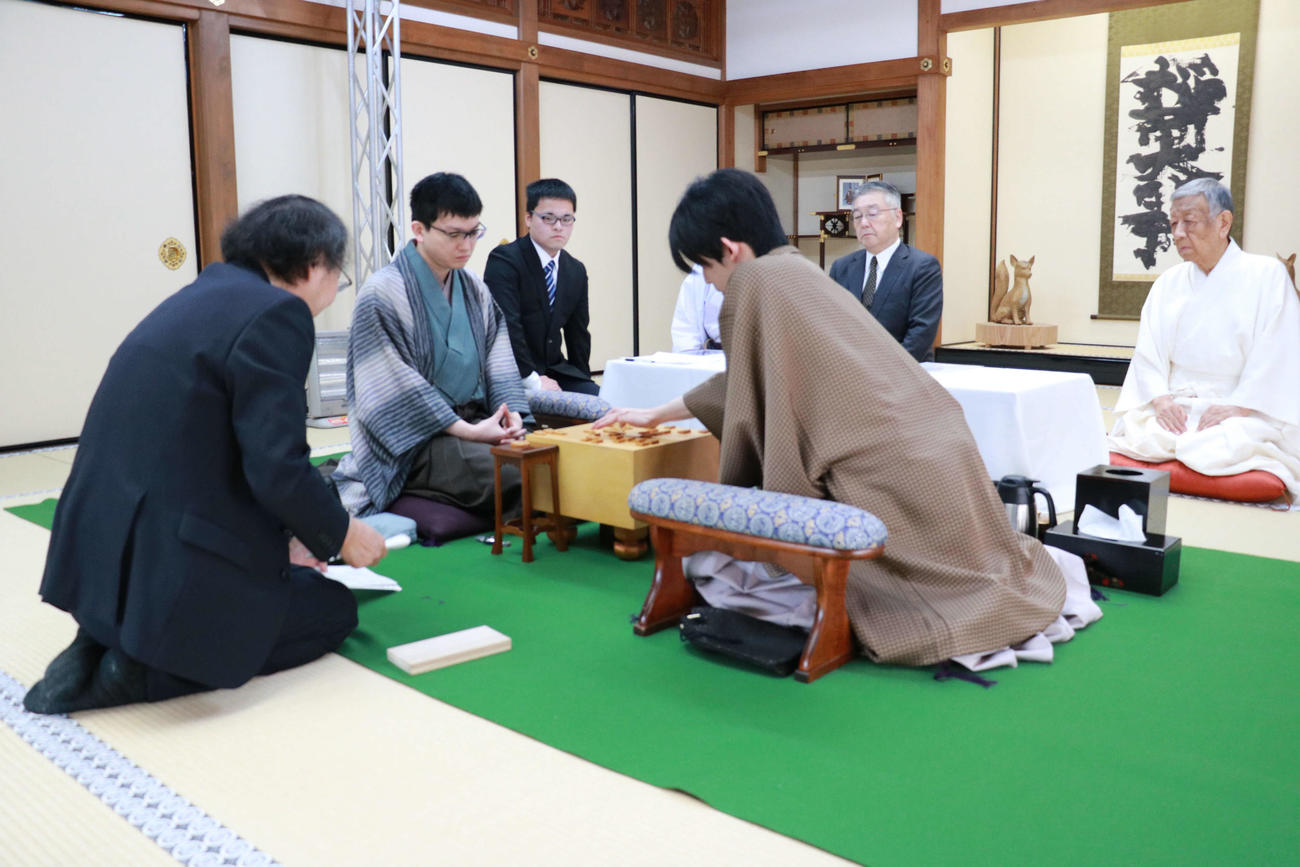 立会人の福崎文吾九段（左）によって開封された封じ手を指す藤井聡太王将（右、中央は永瀬拓矢九段＝日本将棋連盟提供）