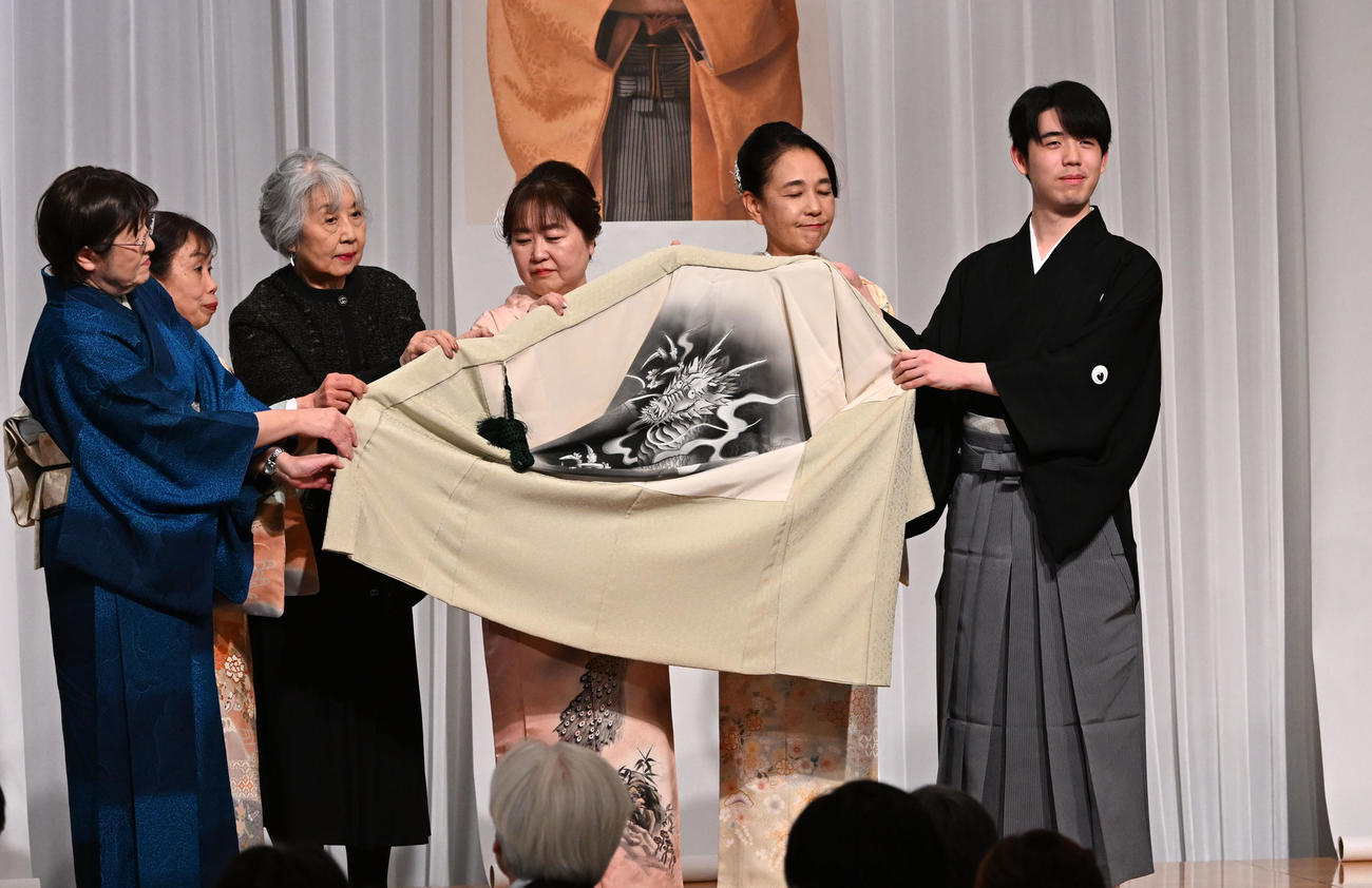 第38期竜王就位式　クラウドファンディングの支援者と贈られた記念の羽織を広げる藤井竜王（右端）（撮影・千葉一成）