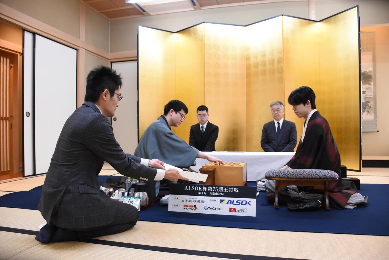 立会人の稲葉陽八段（左）が手で示す永瀬拓矢九段の封じ手を確認する藤井聡太王将（右）（日本将棋連盟提供）