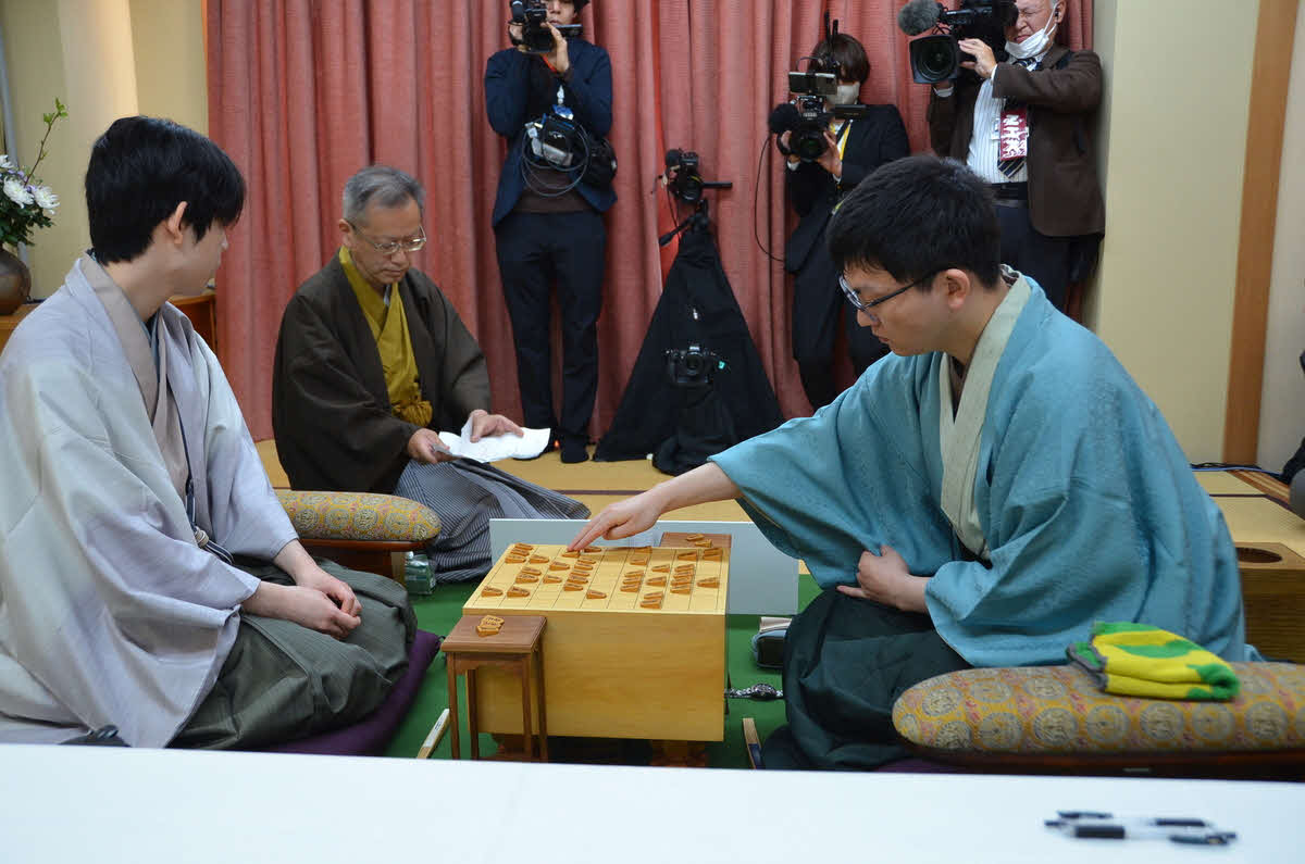王将戦第5局は永瀬拓矢九段（右）の封じ手を立会人の中村修九段（中央）が開封して再開（左は藤井聡太王将、日本将棋連盟提供）