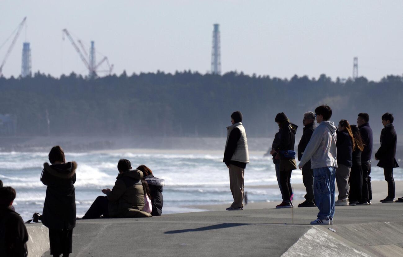 東日本大震災から15年、地震発生時刻に合わせ、海に向かって黙とうする人たち。奥は東京電力福島第1原発の排気筒（共同）