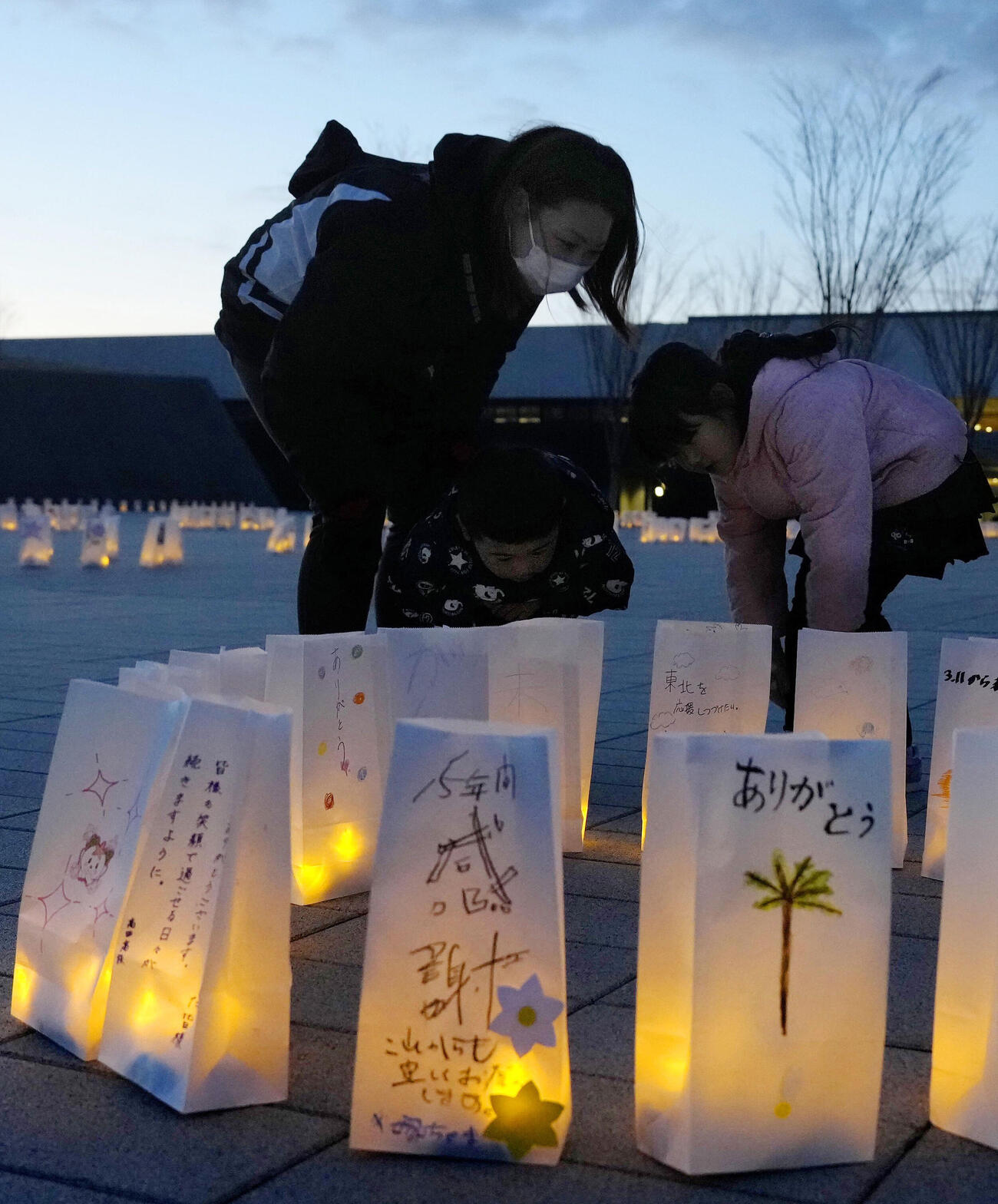 岩手県陸前高田市の高田松原津波復興祈念公園で明かりが灯ったランタン入りの紙袋を見つめる親子（共同）