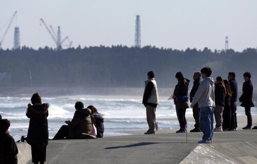 東日本大震災から15年、地震発生時刻に合わせ、海に向かって黙とうする人たち。奥は東京電力福島第1原発の排気筒（共同）
