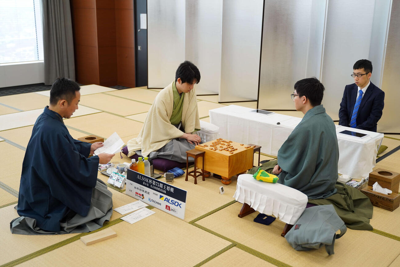 王将戦7番勝負第6局2日目に臨んだ藤井聡太王将（中央）永瀬拓矢九段（右）、封じ手を読み上げる屋敷伸之九段（日本将棋連盟提供）
