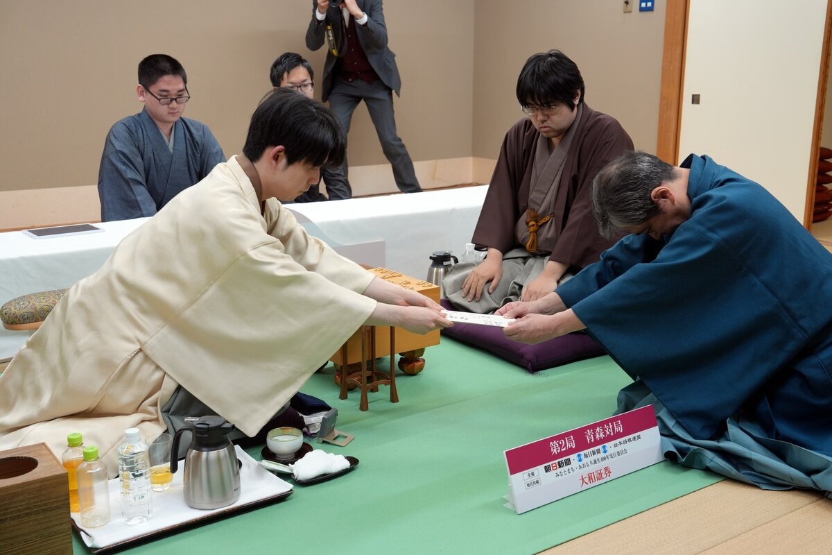 藤井聡太名人（左）は封じ手の入った封筒を立会人の行方尚史九段に渡す。中央は挑戦者の糸谷哲郎九段（日本将棋連盟提供）