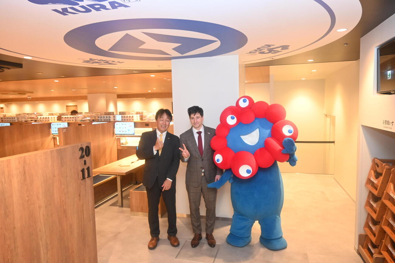大阪・関西万博会場内に出店した店舗を再現した新店舗「くら寿司　メモリアル店　なんば千日前」の内覧会に出席した左からくら寿司の岡本浩之取締役、在大阪ハンガリー領事館、ケレケシュ・アンドラーシュ領事館長、ミャクミャク（撮影・松浦隆司）