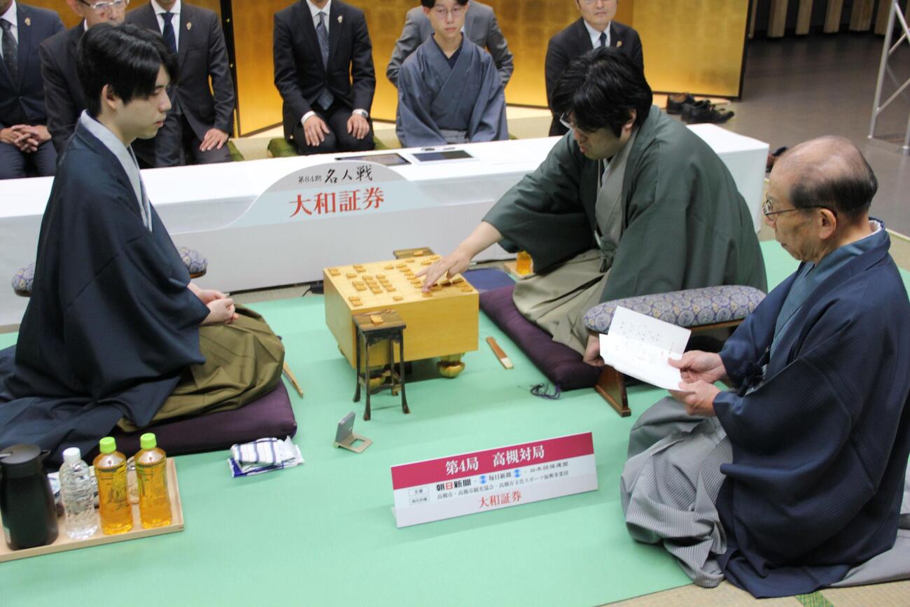 立会人の桐山清澄九段（右）が読み上げる封じ手を指す糸谷哲郎九段（中央）、藤井聡太名人（左）（日本将棋連盟提供）