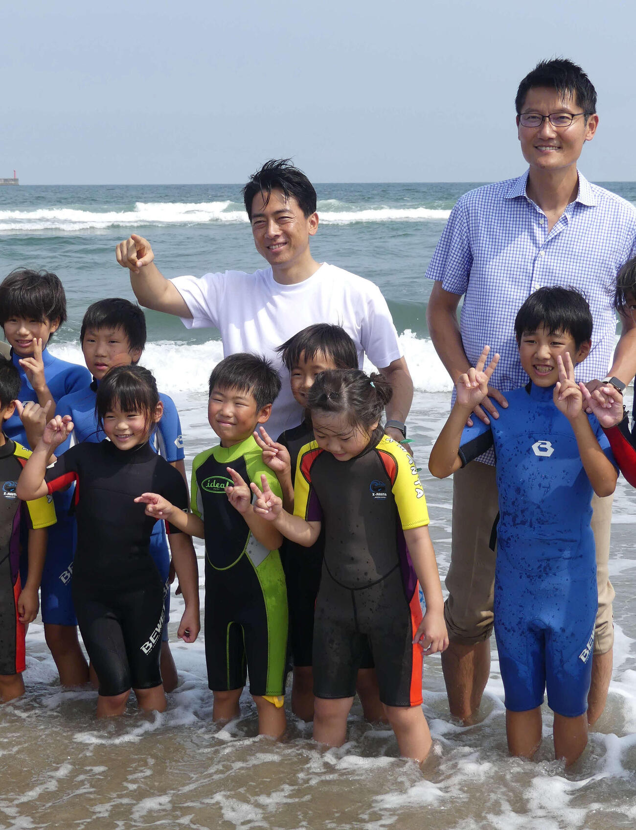 サーフィンを楽しむ子どもたちとふれあう小泉進次郎元環境相（後列中央）。同右は朝日健太郎環境政務官（2023年9月撮影）