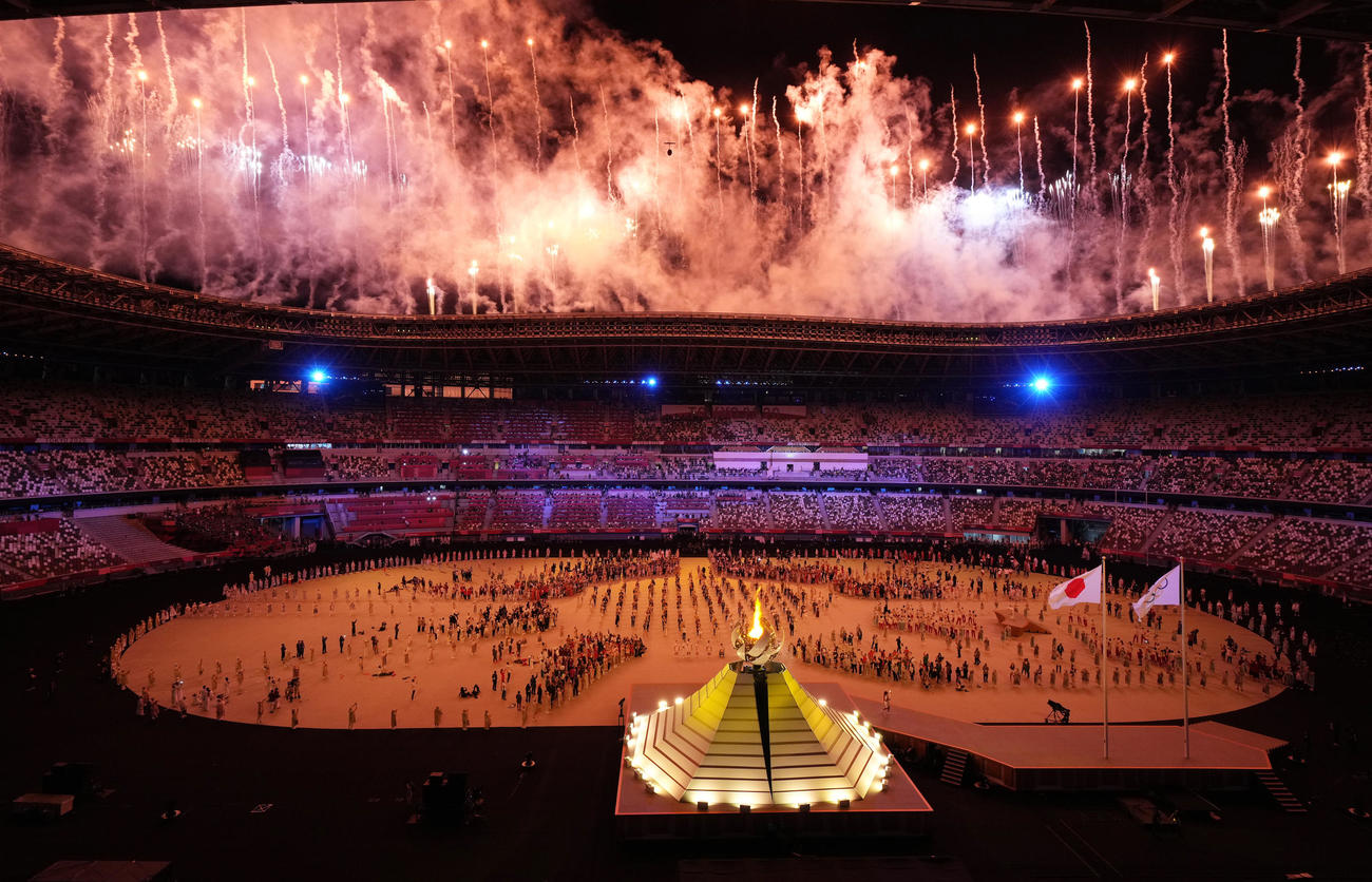 東京五輪開会式で聖火台に火がともされ、祝福の花火が打ち上げられる