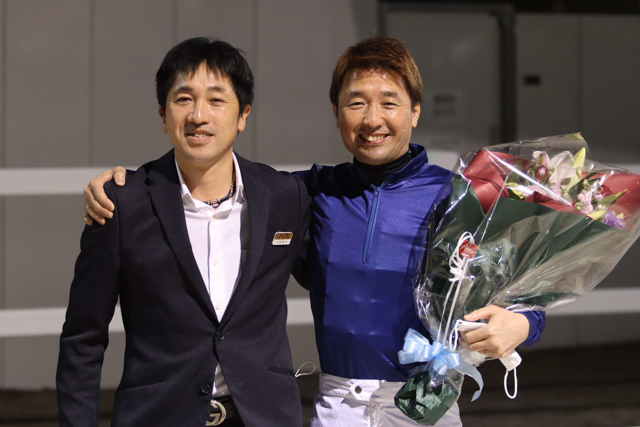 山田信大調教師（左）から花束を贈られ笑顔の酒井忍騎手