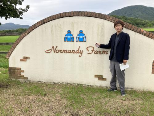 ノルマンディーファームの看板とともに写真に納まる井上記者