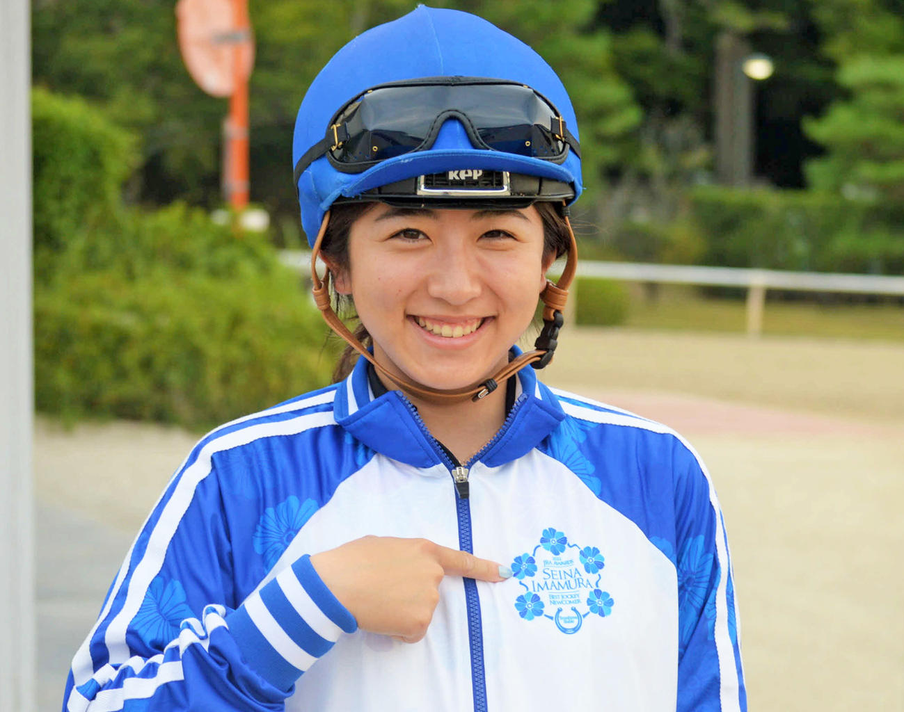 新人賞を記念して作成したオリジナルブルゾンのロゴを指さす今村聖奈騎手