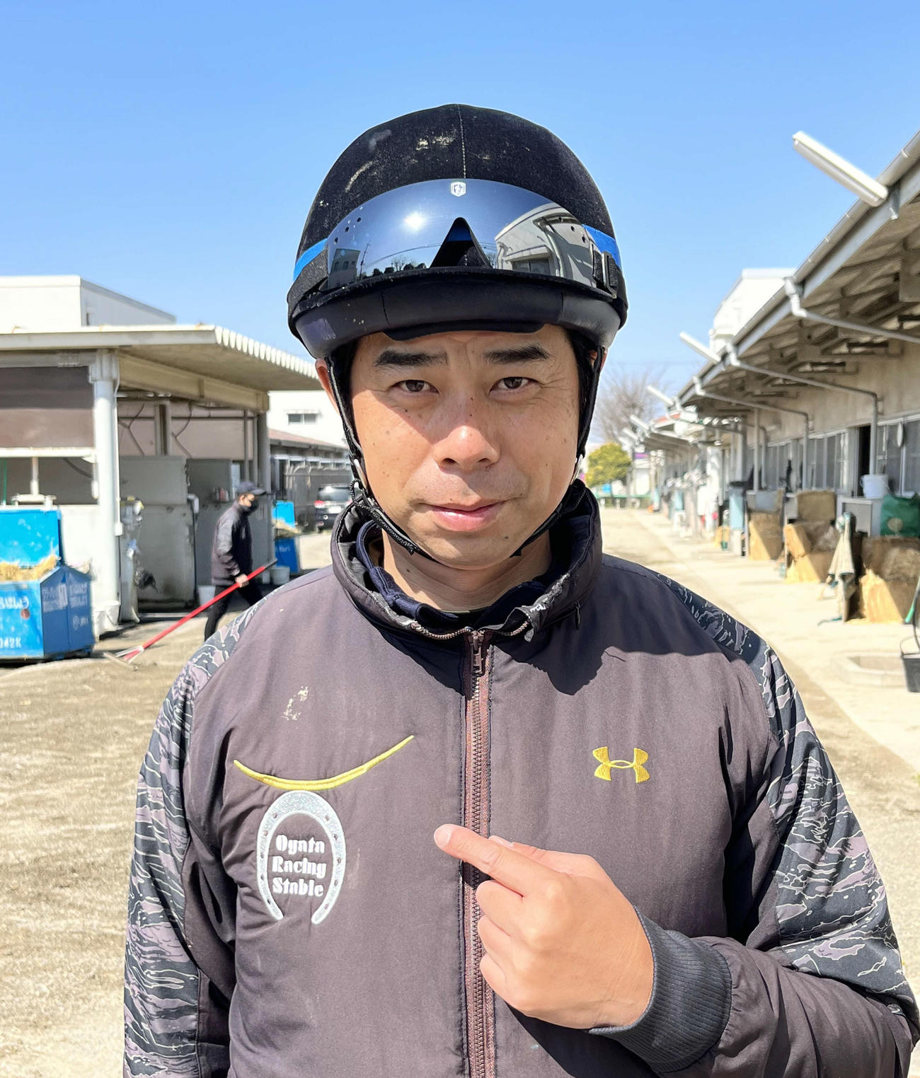 伊達政宗のかぶとをイメージした厩舎のロゴを指す尾形師（2022年4月撮影）