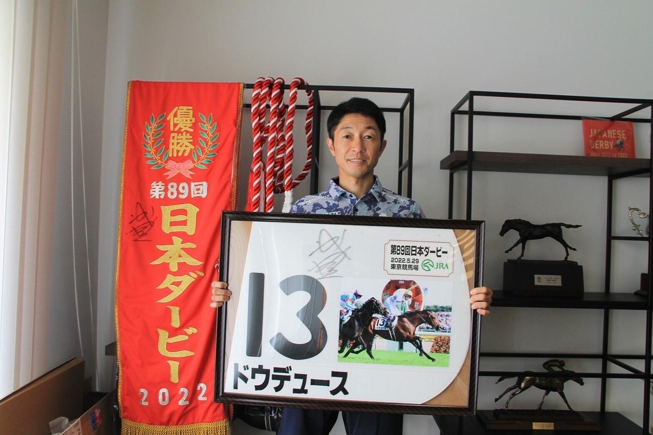 ダービー優勝ゼッケンのレプリカを持つ武豊騎手（キーファーズサロン提供）