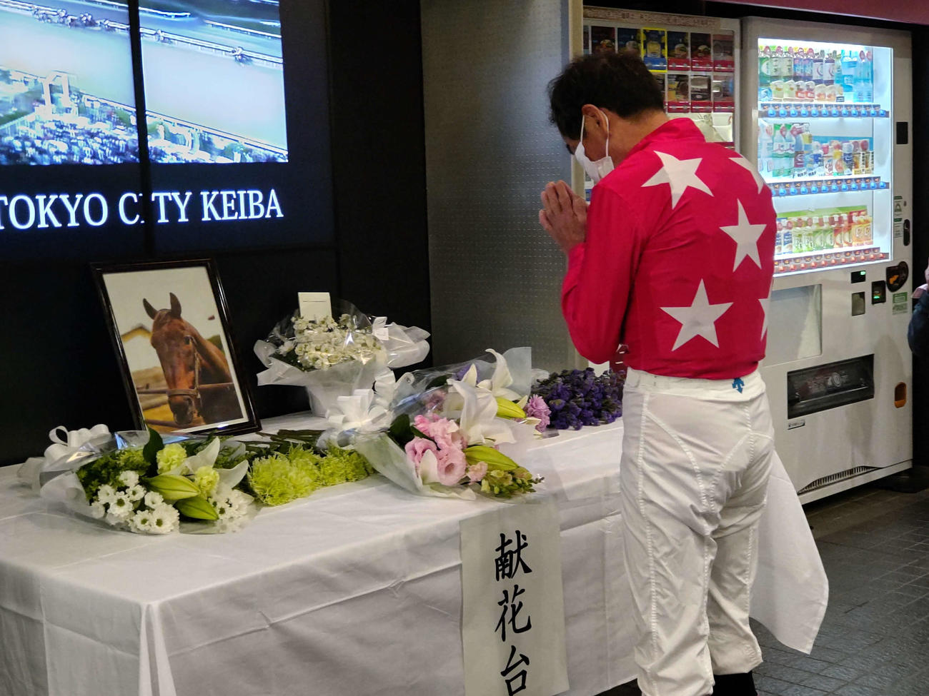 コンサートボーイの献花台に花を手向け手を合わせる的場文男騎手