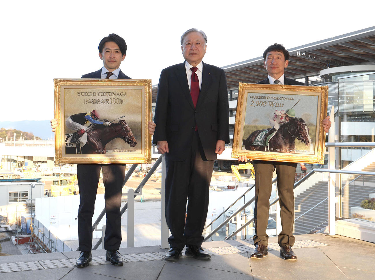 建設中の京都競馬場新スタンドをバックに記念撮影に納まる左から福永騎手、後藤JRA理事長、横山典騎手