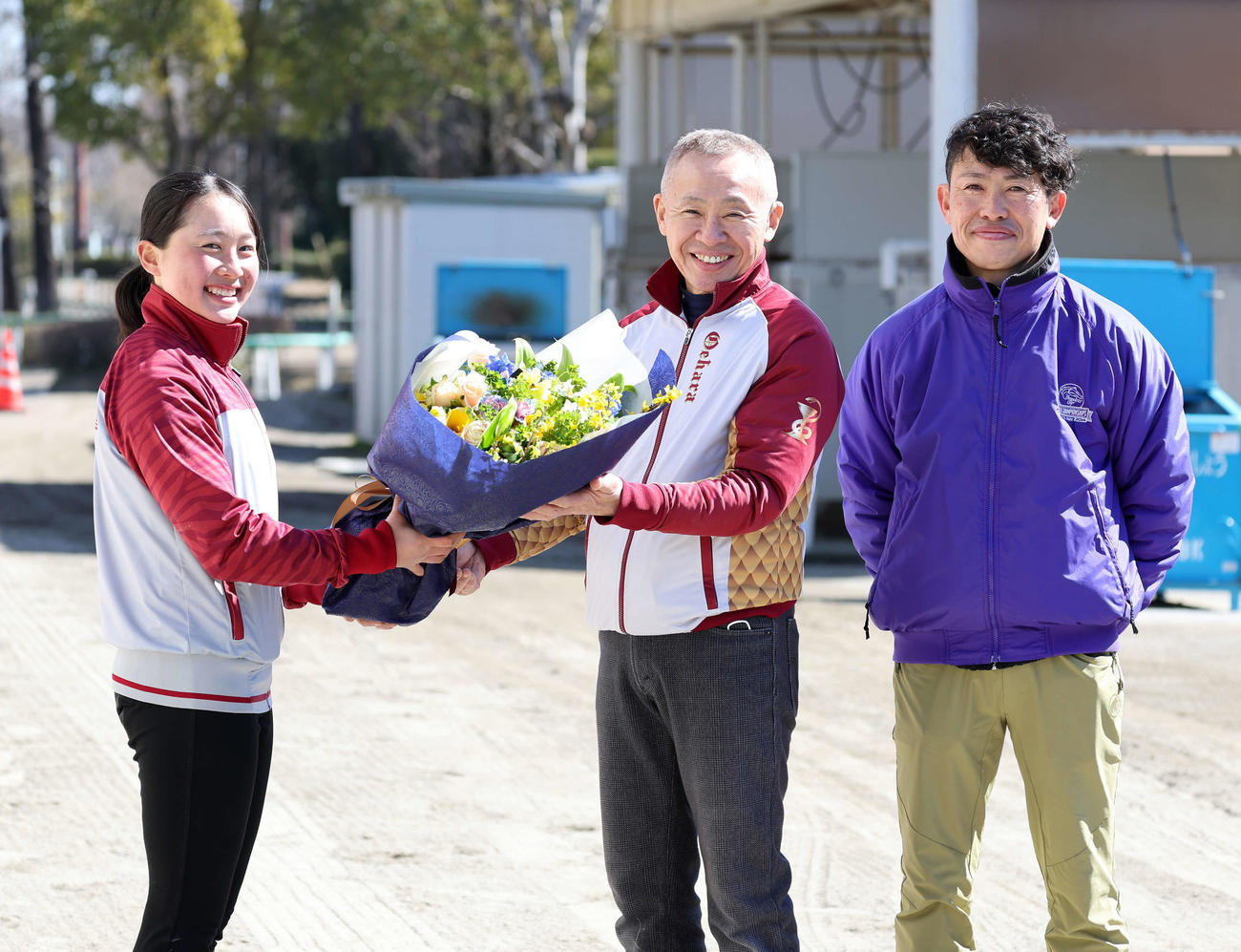 競馬学校騎手課程に在籍する孫の比呂さん（左）から花束を受け取る大江原調教師。右は長男の勝氏（撮影・鈴木正人）