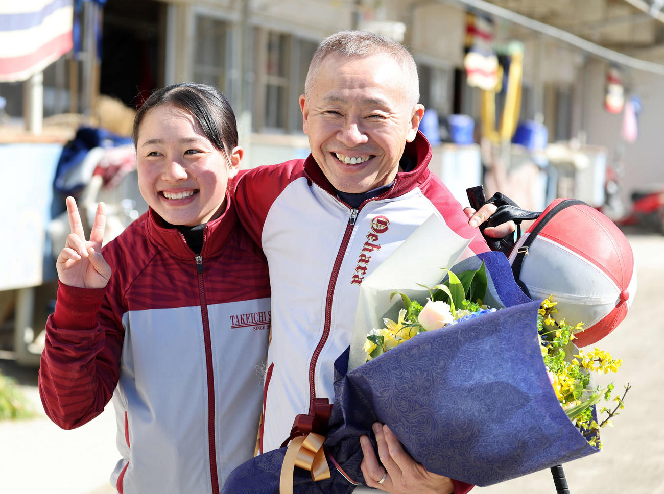 競馬学校騎手課程に在籍する孫の比呂さん（左）から花束を受け取り笑顔を見せる大江原調教師（撮影・鈴木正人）